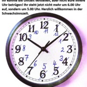 Eine analoge Wanduhr zeigt 10:08 Uhr an. Die Ziffern wurden handschriftlich um eine Stunde zurückkorrigiert, um auf die ursprüngliche Zeit vor der Umstellung auf Sommerzeit hinzuweisen. Über der Uhr steht ein ironischer Text: „Ihr könntet die Uhrzeit verstellen, aber nicht eure innere Uhr betrügen! Ihr steht jetzt nicht mehr um 6.00 Uhr auf, sondern um 5.00 Uhr. Herzlich willkommen in der Schwachsinnszeit.“